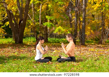 An attractive  man and woman practice Yoga padmasana pose in forest