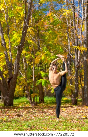 Man exercises in the autumn forest yoga Trivikrama Sana pose