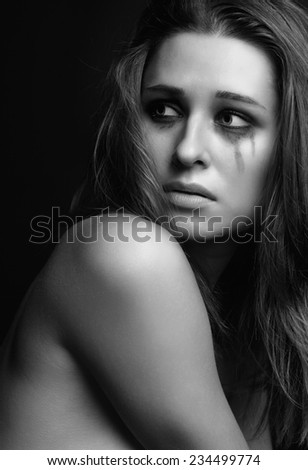 Young pretty woman with smeared mascara crying on black background