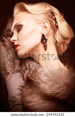Young blonde woman in black dress and fur of silver fox on dark background toned in marsala color