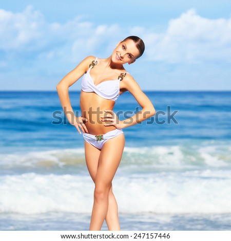 portrait of young beautiful smiling woman in white bikini posing on sea background