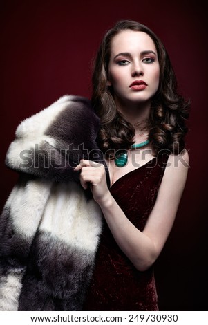 Young blonde woman in black dress and fur coat on dark red marsala background