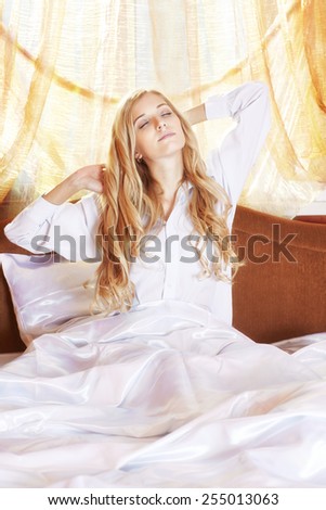 Young beautiful blonde in the bed at morning time stretching hands up with closed eyes