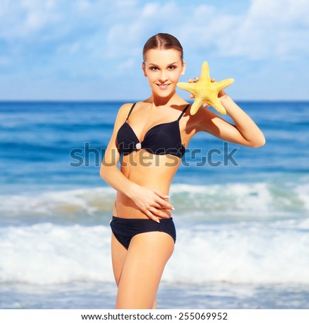 portrait of young beautiful woman in black bikini posing with sea-star on sea background