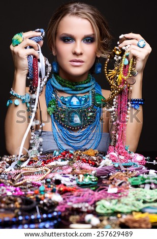 Portrait of young beautiful woman over heap of bijouterie on the table with beads in hands