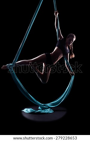 Young woman gymnast with blue gymnastic aerial silks isolated on black
