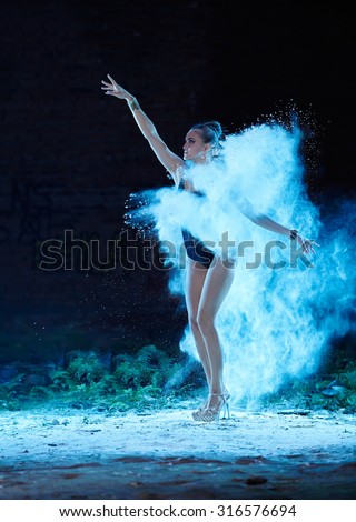 Young woman jumping in blue powder cloud on deserted factory grunge background