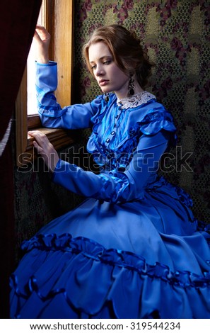 Young woman in blue vintage dress late 19th century sitting in coupe near the window of retro railway vehicle