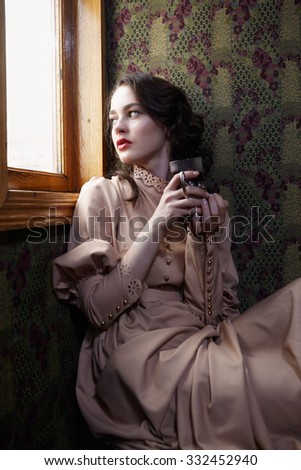 Young woman in beige vintage dress of early 20th century drinking tea in coupe of retro railway train