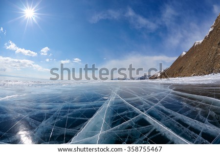 Wide angle shot of winter ice landscape on Siberian lake Baikal with dramatic weather clouds on blue sky background