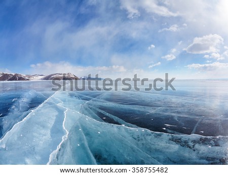 Wide angle shot of winter ice landscape on Siberian lake Baikal with dramatic weather clouds on blue sky background