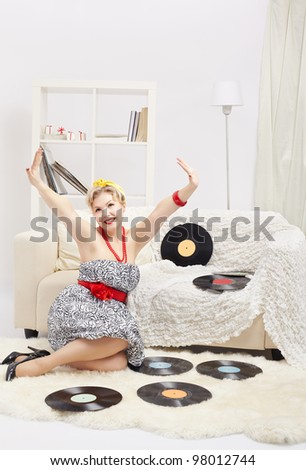 indoor portrait of beautiful young happy blonde size plus woman model sitting on fur carpet with vinyl records around in interior