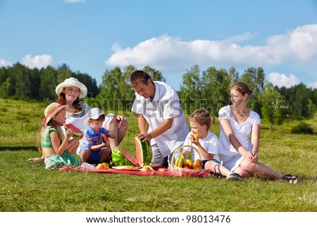 outdoor group portrait of happy family having picnic on green grass in park. father is cutting watermelon.