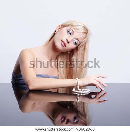 portrait of young beautiful long-haired blonde woman sitting with pearl necklace at reflecting table