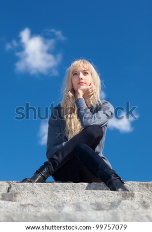 Beautiful young woman sitting on the stone steps in the sky