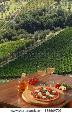 Italian pizza and glasses of white wine in Chianti, famous vineyard landscape in Italy