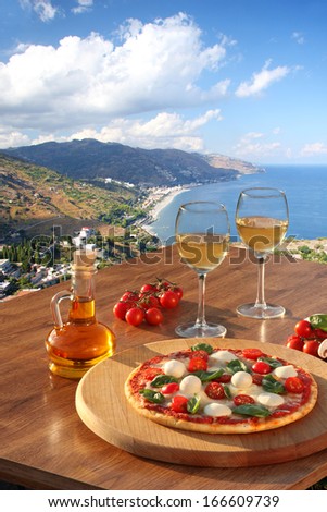 Taormina village with Italian pizza and glasses of wine on the table against sea view, Sicily island, Italy