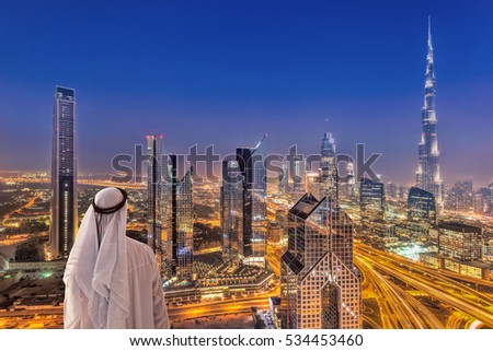 Arabian man watching night cityscape of Dubai with modern futuristic architecture in United Arab Emirates,