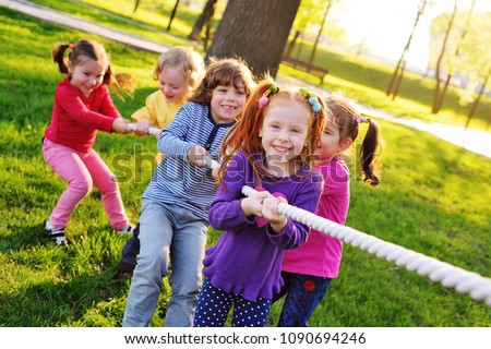 a group of small preschool children play a tug of war in the park. Outdoor games, childhood, friendship, leadership, children\'s day.