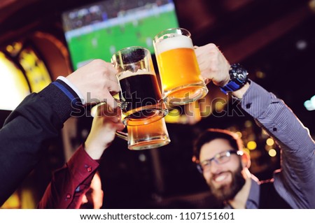 a group of young men's friends in a bar or pub drinking beer with glasses and watching football during the celebration of Oktoberfest
