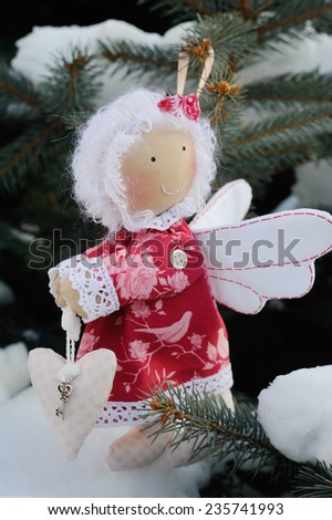 Christmas tree toy angel with heart in hands. Christmas Toy angel hung on a pine tree. Snow on the branches of a pine