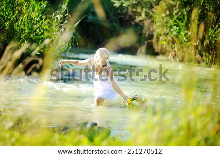 girl in a white sundress on the river starts a wreath of flowers.