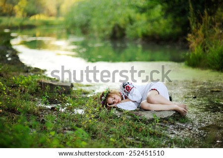 girl in the Ukrainian national clothes with wreaths of flowers on the riverbank