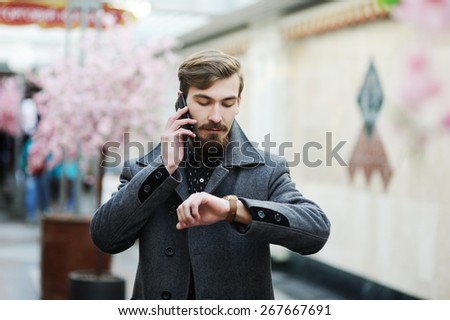 stylish man with a beard and mustache, talking on a cell phone and looks at his watch