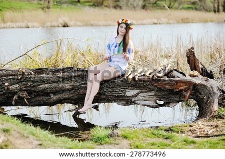 Ukrainian girl in a dress and a wreath of flowers on her head sitting on a log by the river