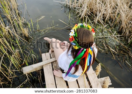 girl in a flower wreath on his head sitting on the bridge and wets feet in the river