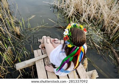 girl in a flower wreath on his head sitting on the bridge and wets feet in the river