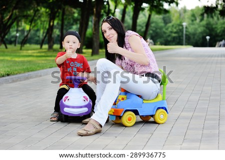 Mother and son driving toy cars hold thumbs up