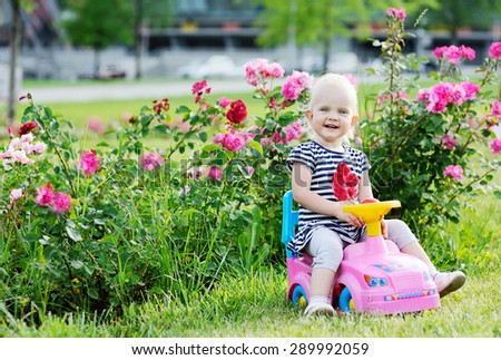 baby girl driving pink toy car on a background of roses