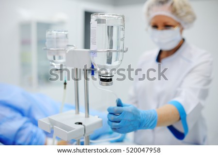 nurse puts the patient medical drip into a vein on the background of the operating room. Dropper against the background of the doctor