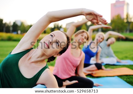 group of people doing yoga on the green with fresh grass outdoors. Healthy lifestyle