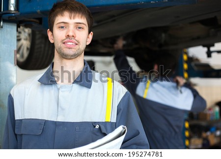 Young repairman auto mechanic inspecting car during automobile maintenance at engine auto repair shop service station