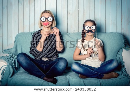 Funny mom and daughter with false mustaches, playing at home