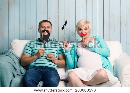 Funny pregnant couple with false mustaches playing at home
