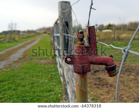 Rusted red tap on a farmers fence post