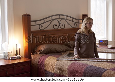 A surreal, altered photo of a girl standing inside a mirror placed on a bed.