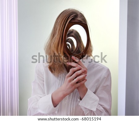 A girl holding a mirror over her face in front of a larger mirror, creating the illusion of infinite reflections.