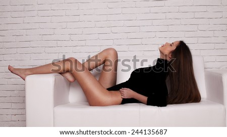 Portrait of beautiful and attractive young adult sensuality and sexy female brunette woman posing in black bikini on the sofa