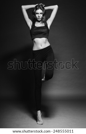 Active beautiful caucasian brunette sexy fitness fashion model with gorgeous athletic body jumping in leggings on one leg in studio for vogue photo shooting promoting health sport lifestyle
