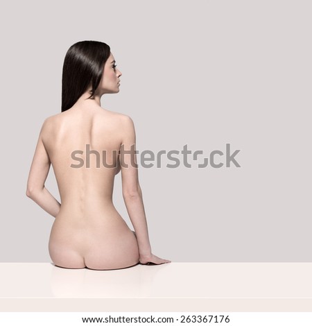 Young European fashion model woman with shiny healthy brunette hair, awesome gorgeous slim body and perfect skin sitting on the table nude in studio for bodycare and wellness advertisement, isolated