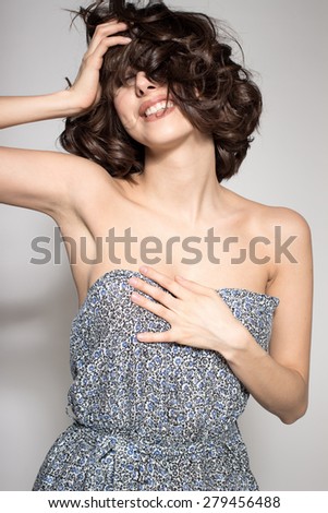 Awesome caucasian attractive joyful happy sexy female model is shaking head with brunette hair in studio wearing nice dress, isolated on gray background