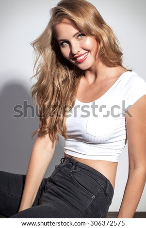 Awesome caucasian attractive sexy professional female model with blond hair posing in studio wearing white shirt and black ripped jeans, smiling, isolated on white background