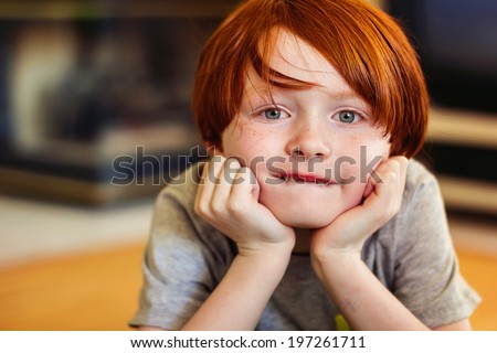A 7 year old redheaded boy holding his head in his hands -- image taken indoors using natural light