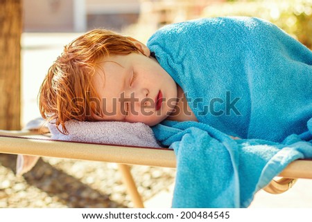 4 year old boy lying on a lounge chair, wrapped in a towel, not feeling well -- image taken outdoors in Reno, Nevada, USA