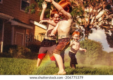 Three young brothers playing in the sprinklers on a hot day -- image taken outdoors in Reno, Nevada, USA