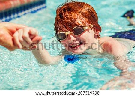 7 year old boy swimming in a pool on a hot summer day with his grandmother reaching her hand out to help him -- image taken outdoors in Reno, Nevada, USA